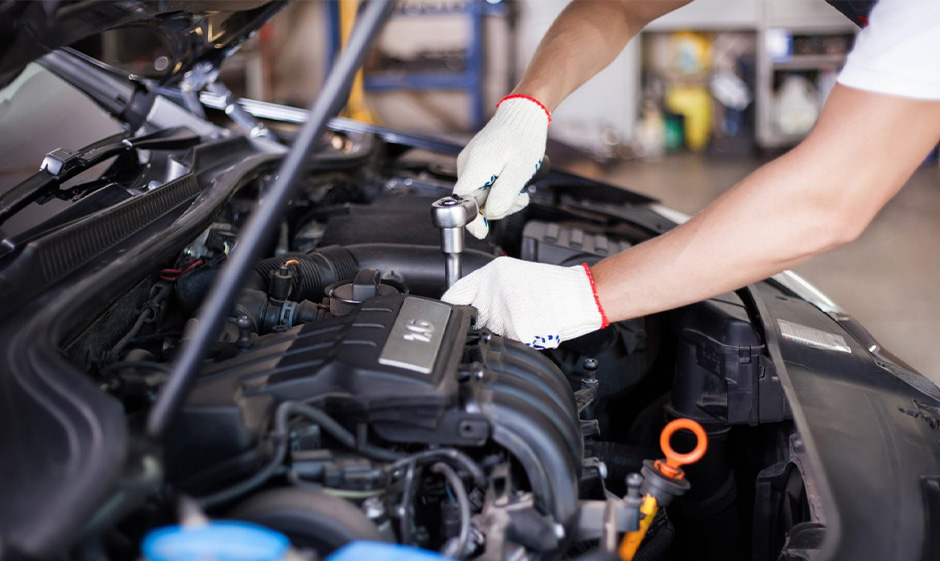 Mechanic under the hood of the car holding a tool